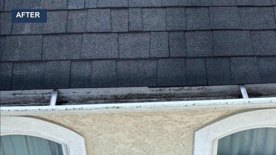 Clean gutter after cleaning, with all dirt and weeds removed above a stucco wall and arched windows