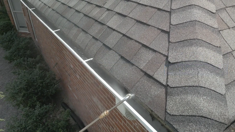 Pressure washer wand flushing a white gutter to clear the last debris during gutter cleaning in Roseville