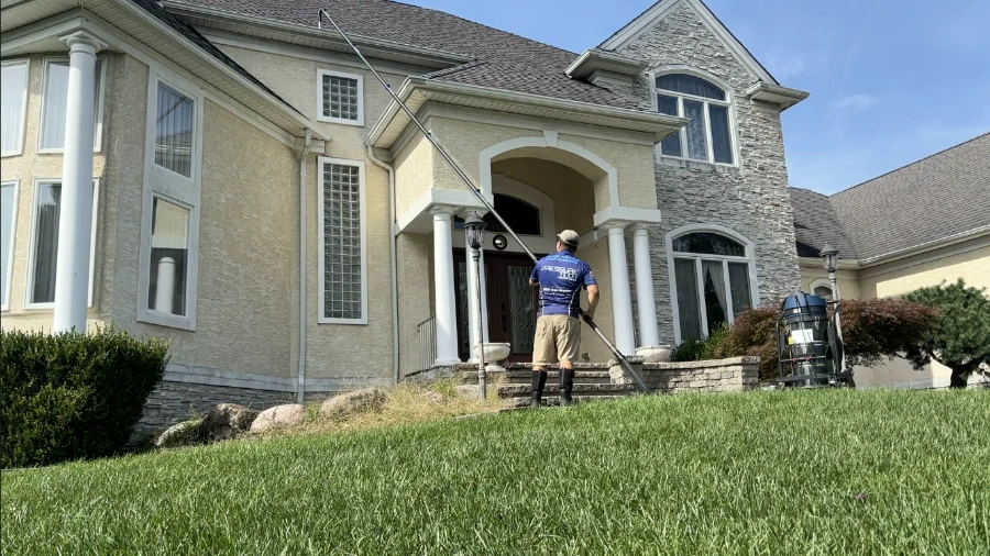 Technician cleaning second-story gutters from the ground with a vacuum pole, one of the safer gutter cleaning tips for two-story homes