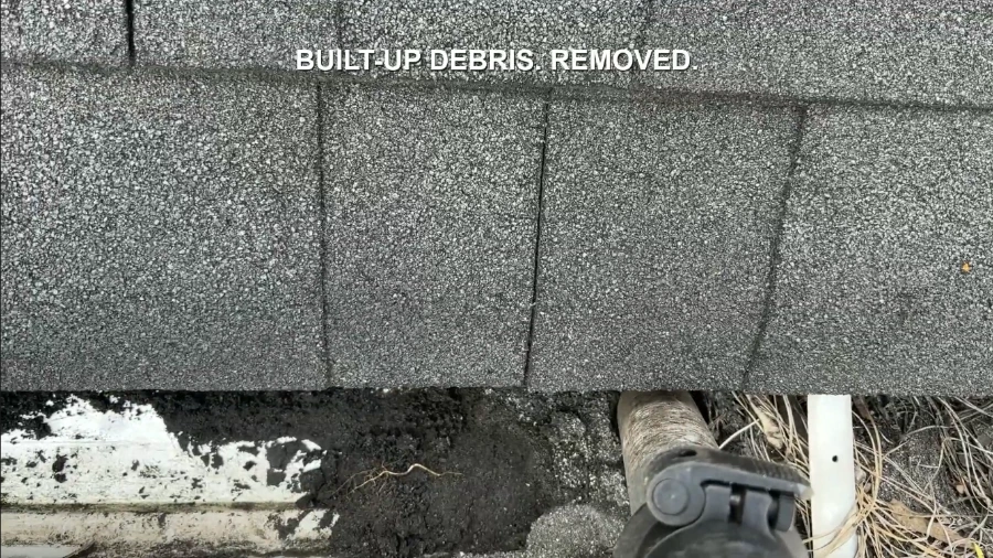 Gutter vacuum hose removing built-up dirt and debris from a clogged gutter during gutter cleaning