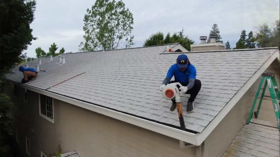 Gutter services in Roseville often start on the roof: a technician uses a leaf blower to clear debris from a two-story home